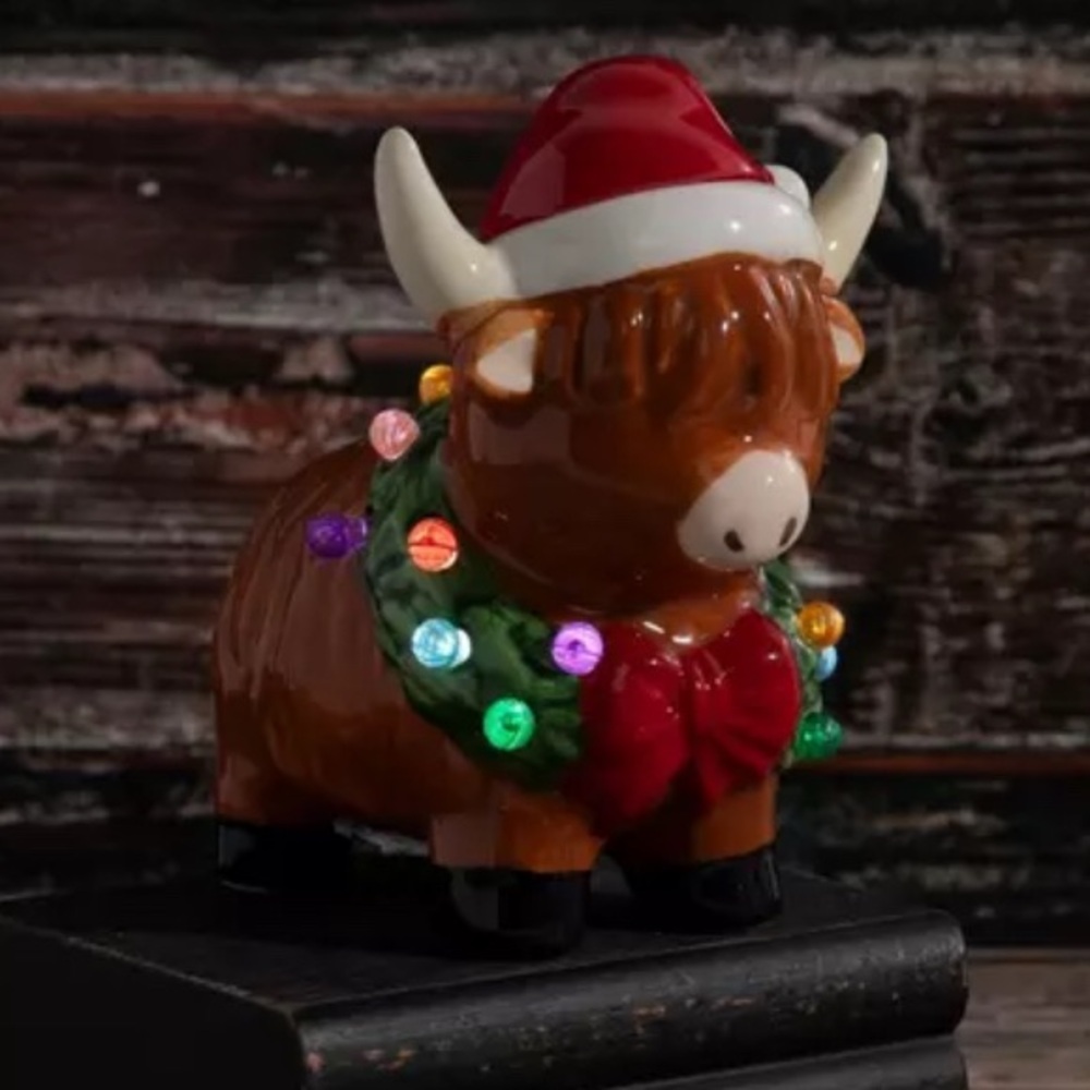 Festive ceramic Highland Cow Holiday Decoration with colorful lights .